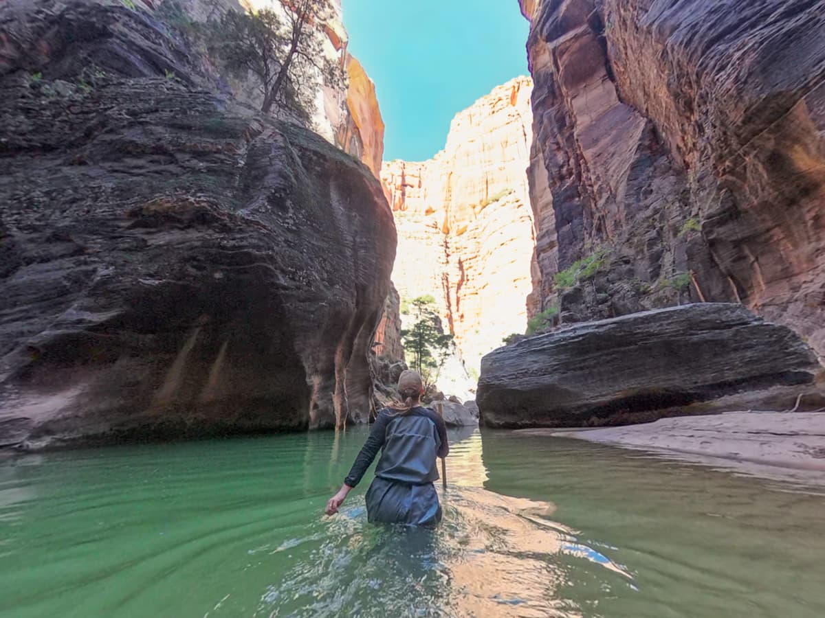 Woman walking through the Virgin River with walls of Zion Canyon in the background along the Narrows Trail in Zion National Park