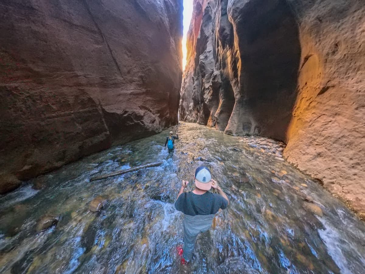 Couple walking through the waters of the Virgin River through a narrow portion of Zion Canyon along The Narrows Trail in Zion National Park