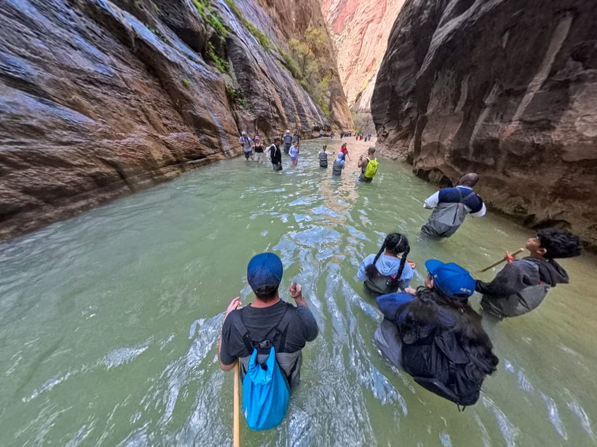 Hikers walking through the Virgin River between canyon walls along The Narrows trail in Zion National Park