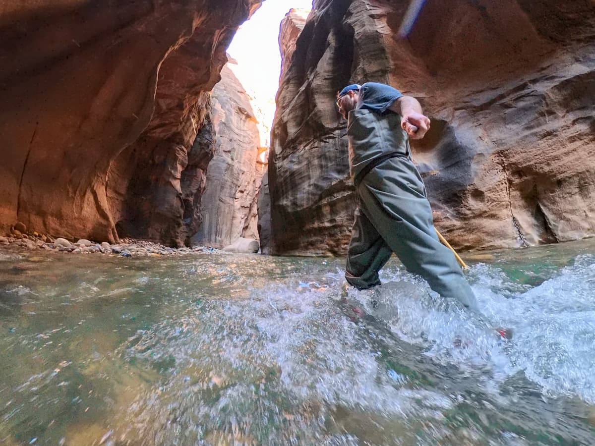 Man walking in the waters of the Virgin River with the walls of Zion Canyon in the background along The Narrows trail in Zion National Park