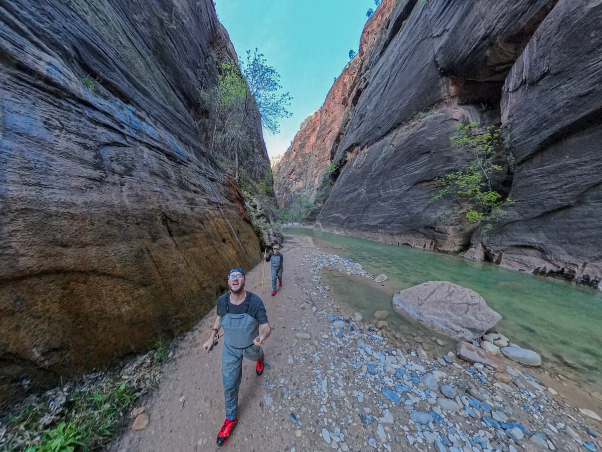 Couple wearing waders while walking on a dry riverbed along The Narrows trail in Zion National Park