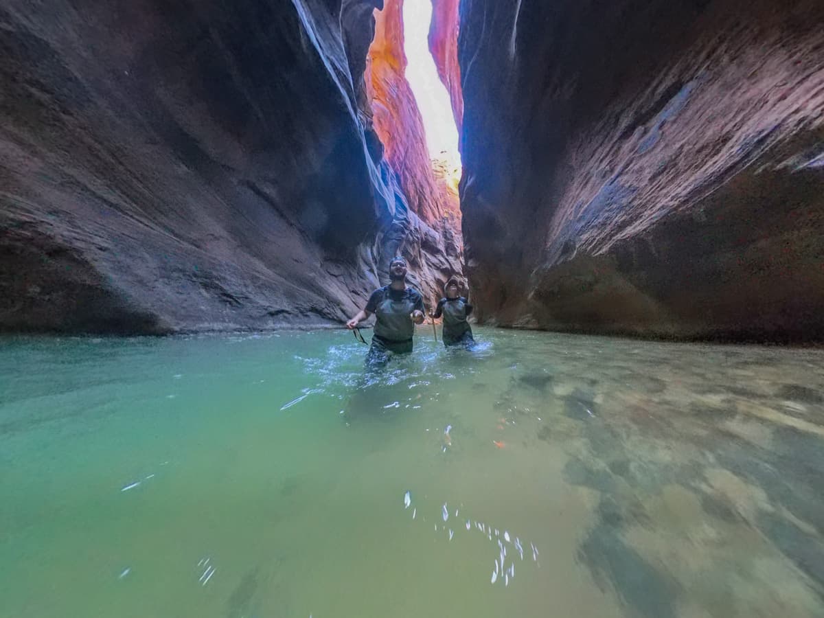 Couple walking through the Virgin River with the walls of Zion Canyon in the background in Zion National Park