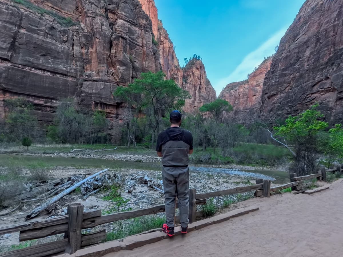 Man wearing waders standing alongside the Riverside Walk with the walls of Zion Canyon in the background in Zion National Park