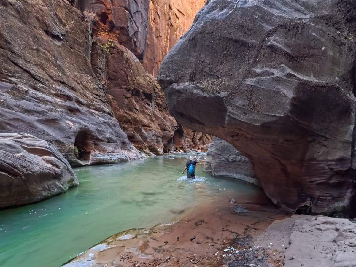 Man walking through the Virgin River with Zion Canyon walls in the background along The Narrows trail in Zion National Park
