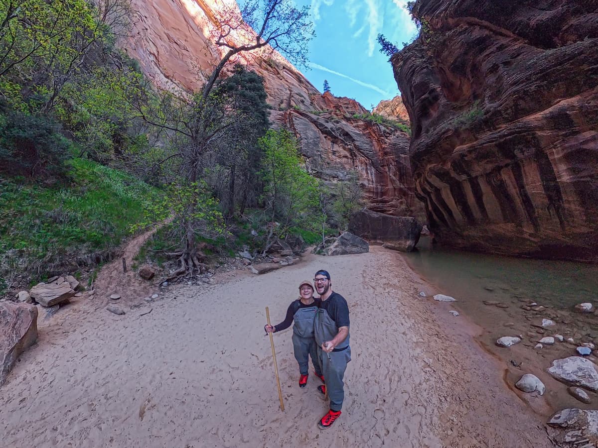 Smiling couple standing on a dry riverbed alongside the Virgin River with walls of Zion Canyon in the background in Zion National Park