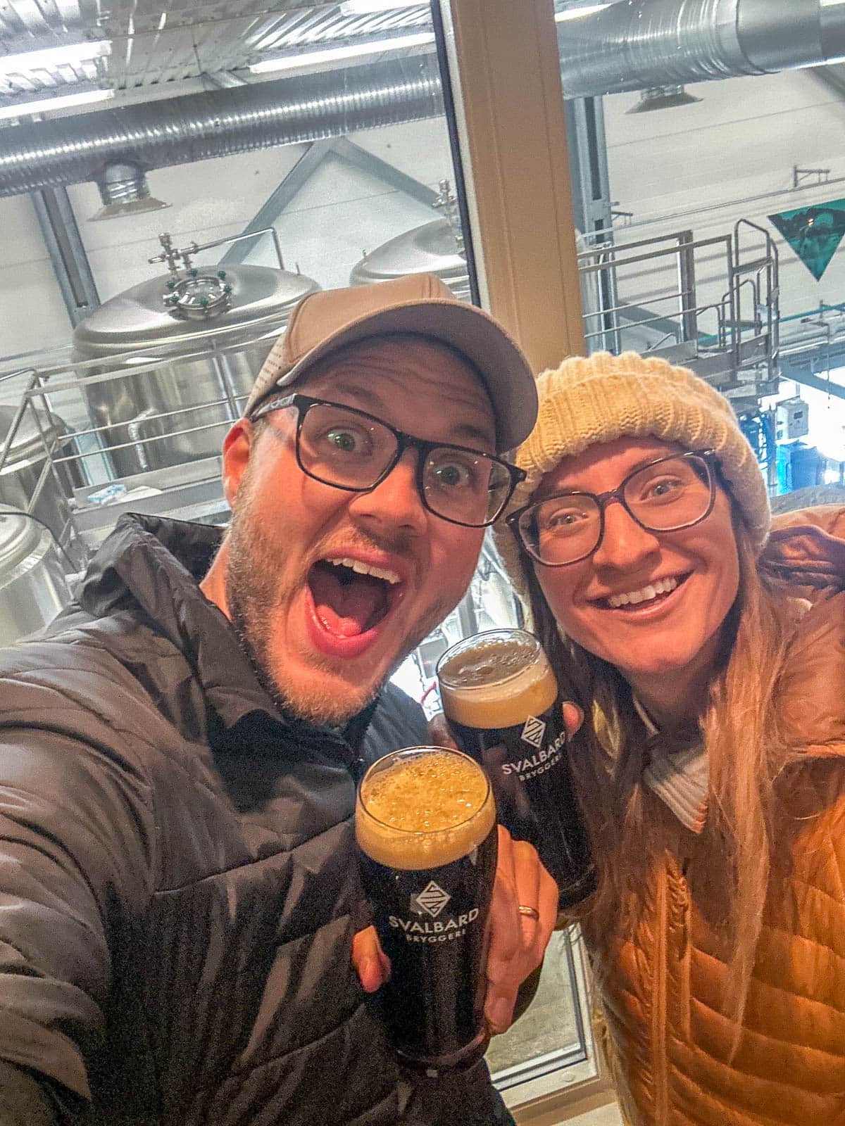 Couple smiling at the Svalbard Brewery in front of brewing equipment in Longyearbyen, Svalbard