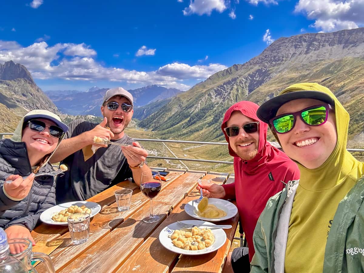 Four smiling friends eating blue cheese gnocchi at Rifugio Elisabetta, Italy along the Tour du Mont Blanc