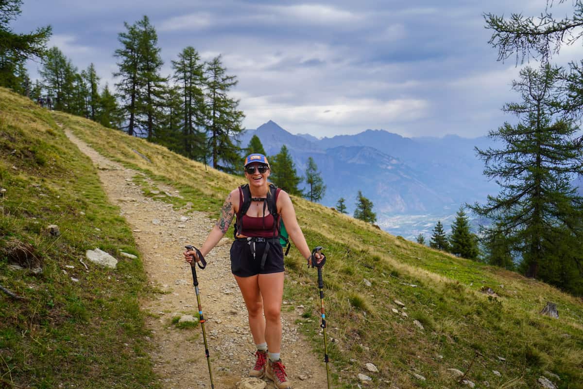 Smiling woman standing on a dirt trail with mountains in the background outside of Trient, Switzerland, along the Tour du Mont Blanc
