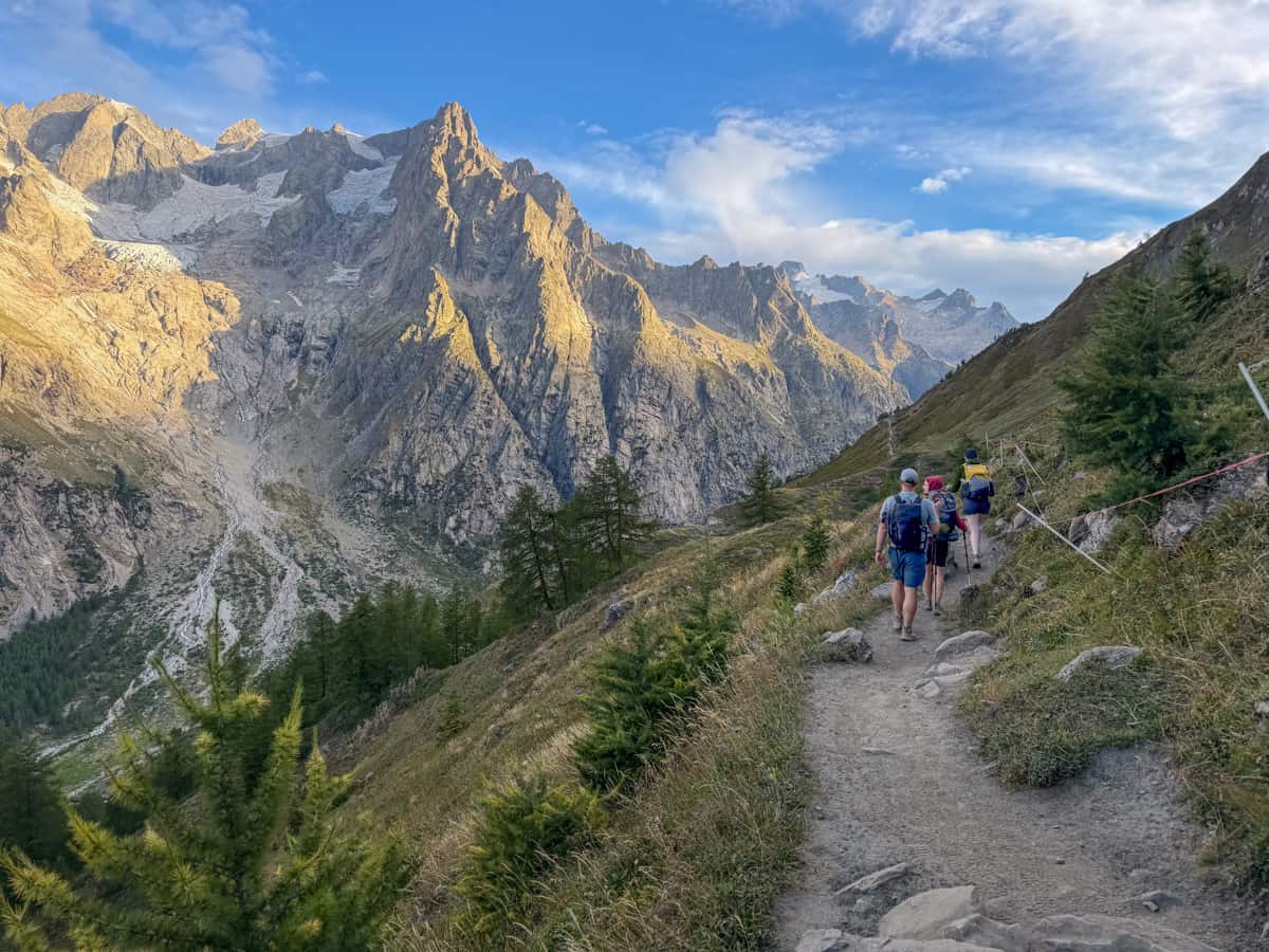 Three friends hiking along a dirt pathway on the Val Ferret with the Italian Alps in the background along the Tour du Mont Blanc