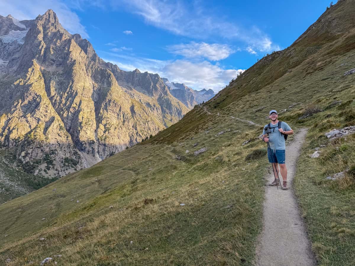 Man hiking along a dirt path with the Italian Alps in the background along the Val Ferret along the Tour du Mont Blanc