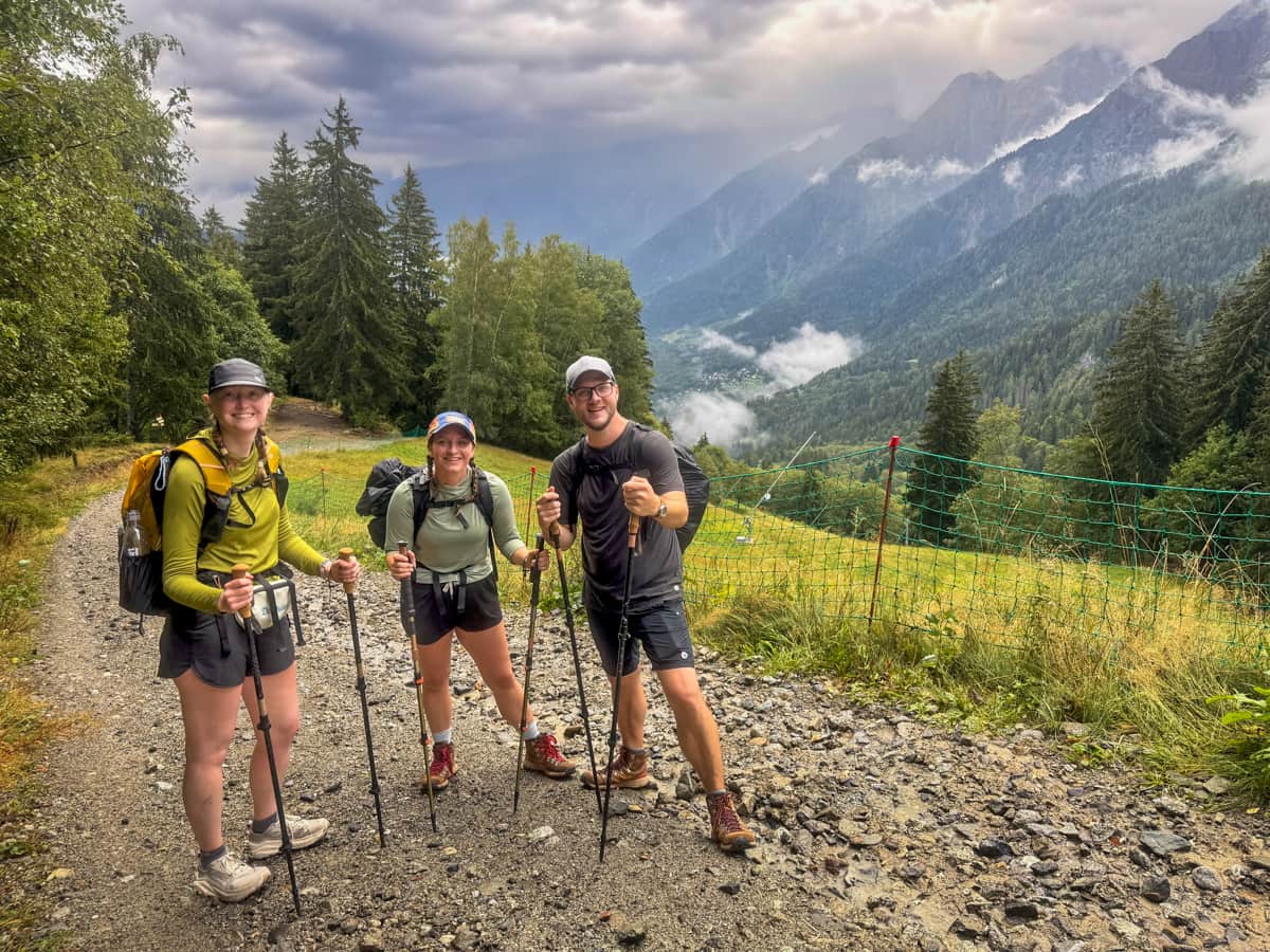 Three smiling friends standing on a gravel pathway with the French Alps in the background in Chamonix, Franace