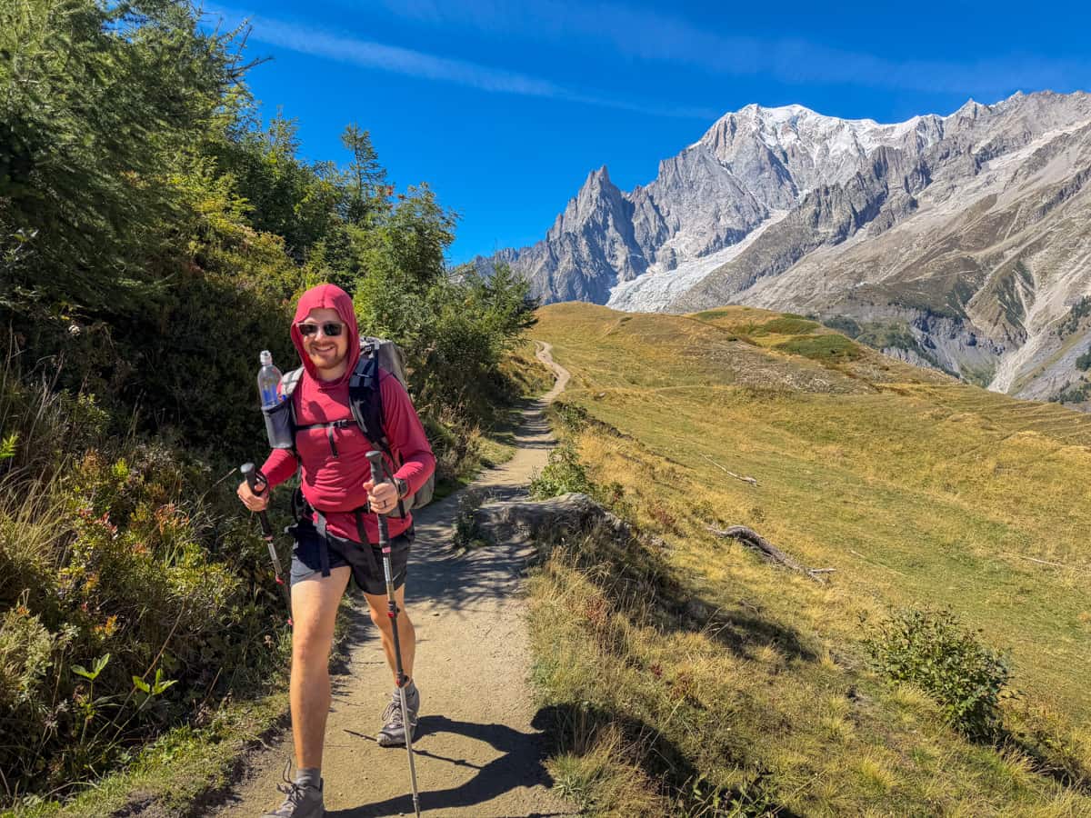 Man hiking along a dirt pathway with the Italian Alps in the background on the Val Ferret of the Tour du Mont Blanc