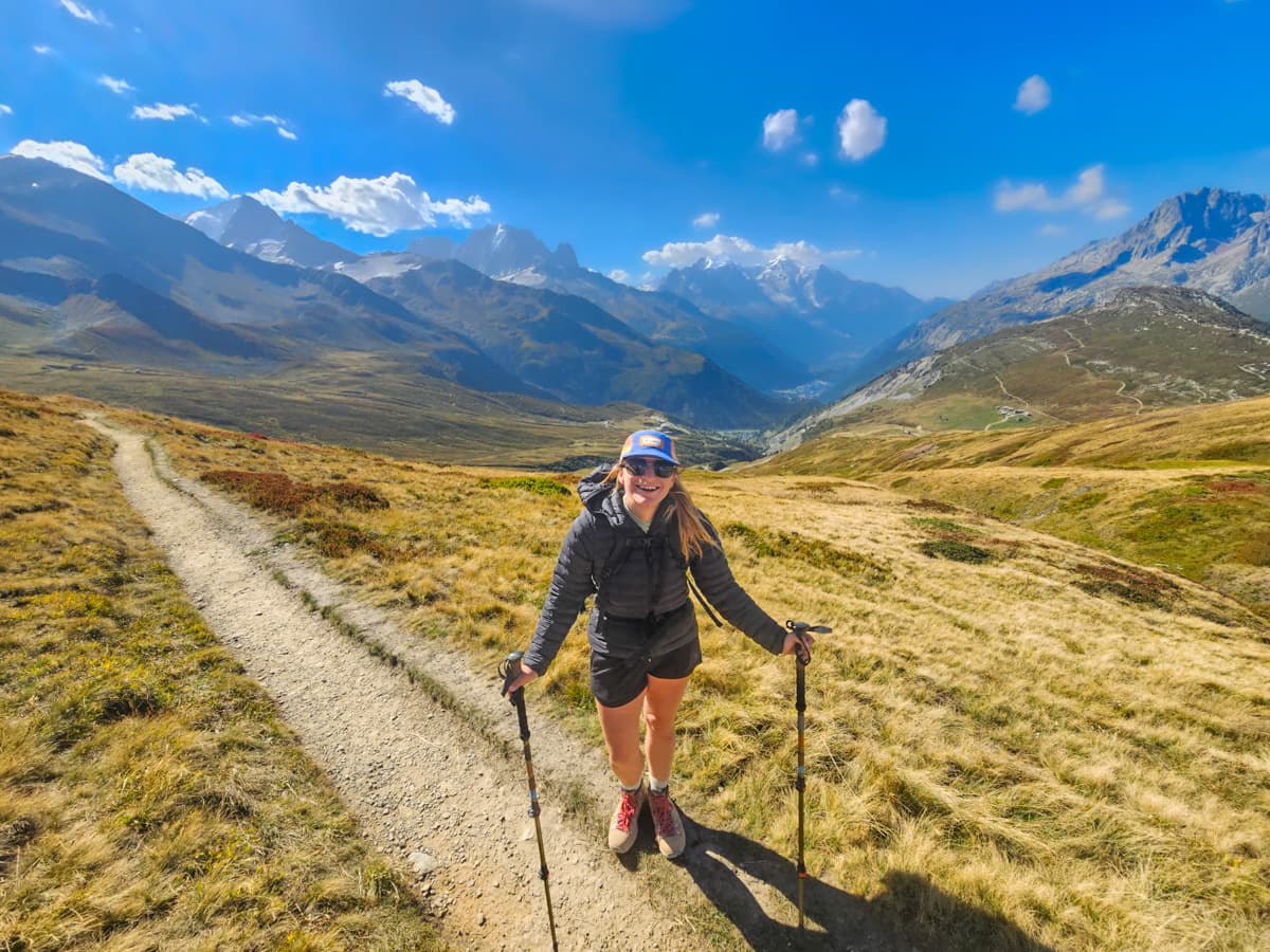 Smiling woman standing on a dirt pathway with Mont Blanc in the background outside of Chamonix, France along the Tour du Mont Blanc
