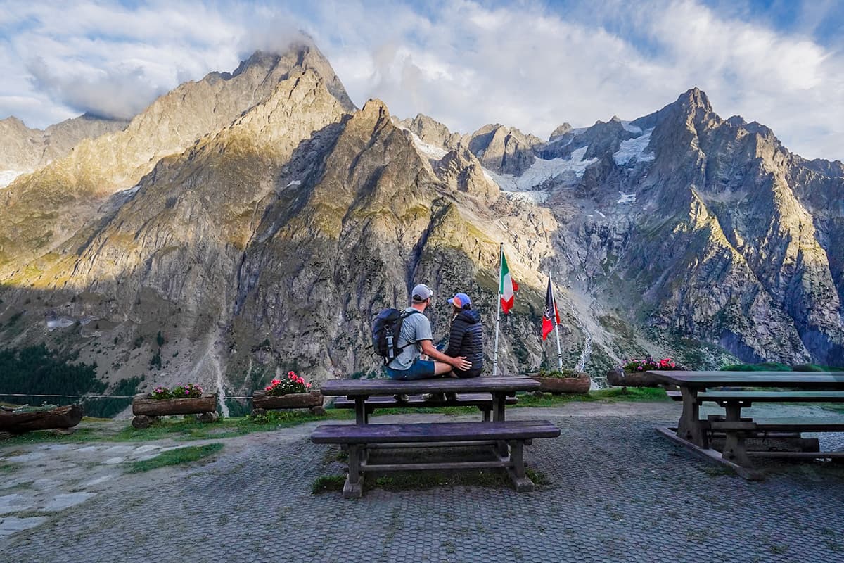 Couple sitting on a picnic table with the Mont Blanc massif in the background at Rifugio Bonatti along the Tour du Mont Blanc
