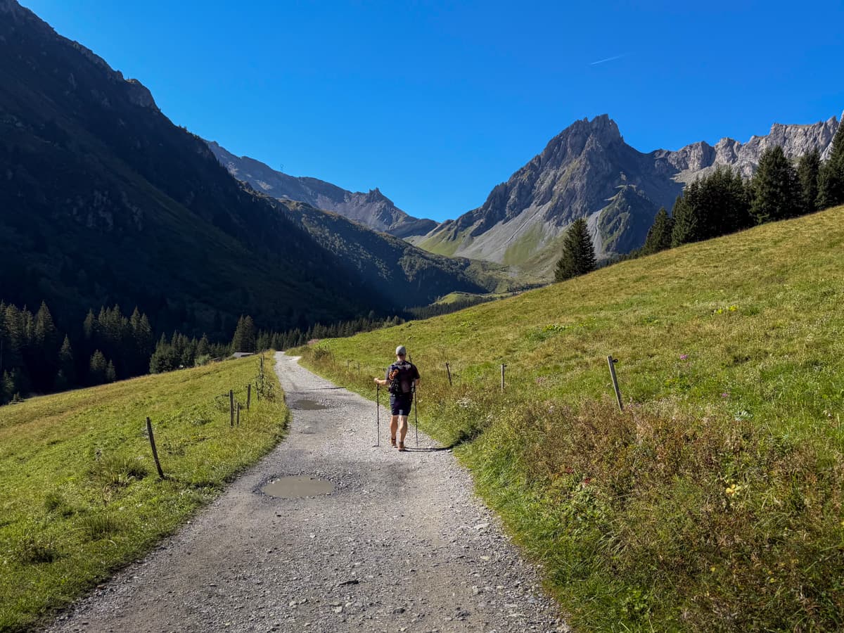 Man hiking along a gravel trail with Aiguilles de la Pennaz in the background along the Tour du Mont Blanc outside of Les Contamines, France