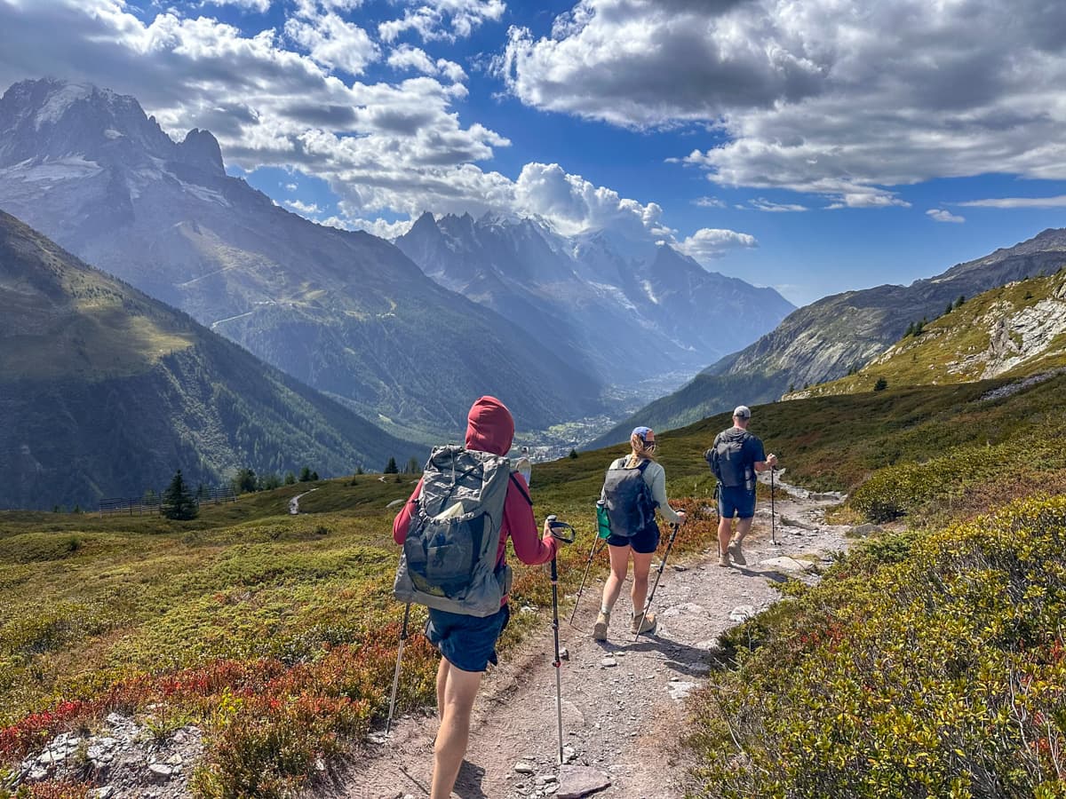 Three hikers hiking through a grassy meadows with the Mont Blanc massif in the background outside of Chamonix, France along the Tour du Mont Blanc