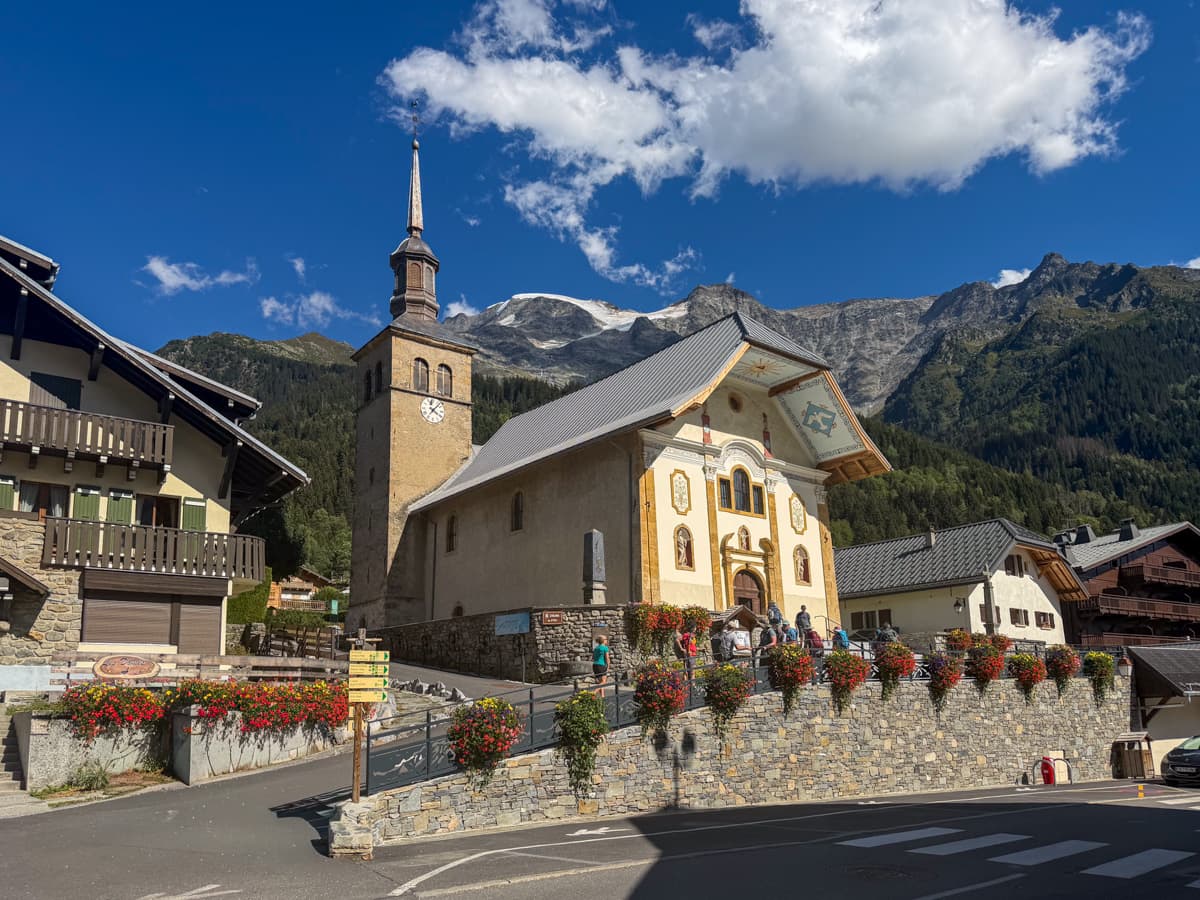 Church and other alpine buildings with the French Alps in the background along the Tour du Mont Blanc in Les Contamines, France