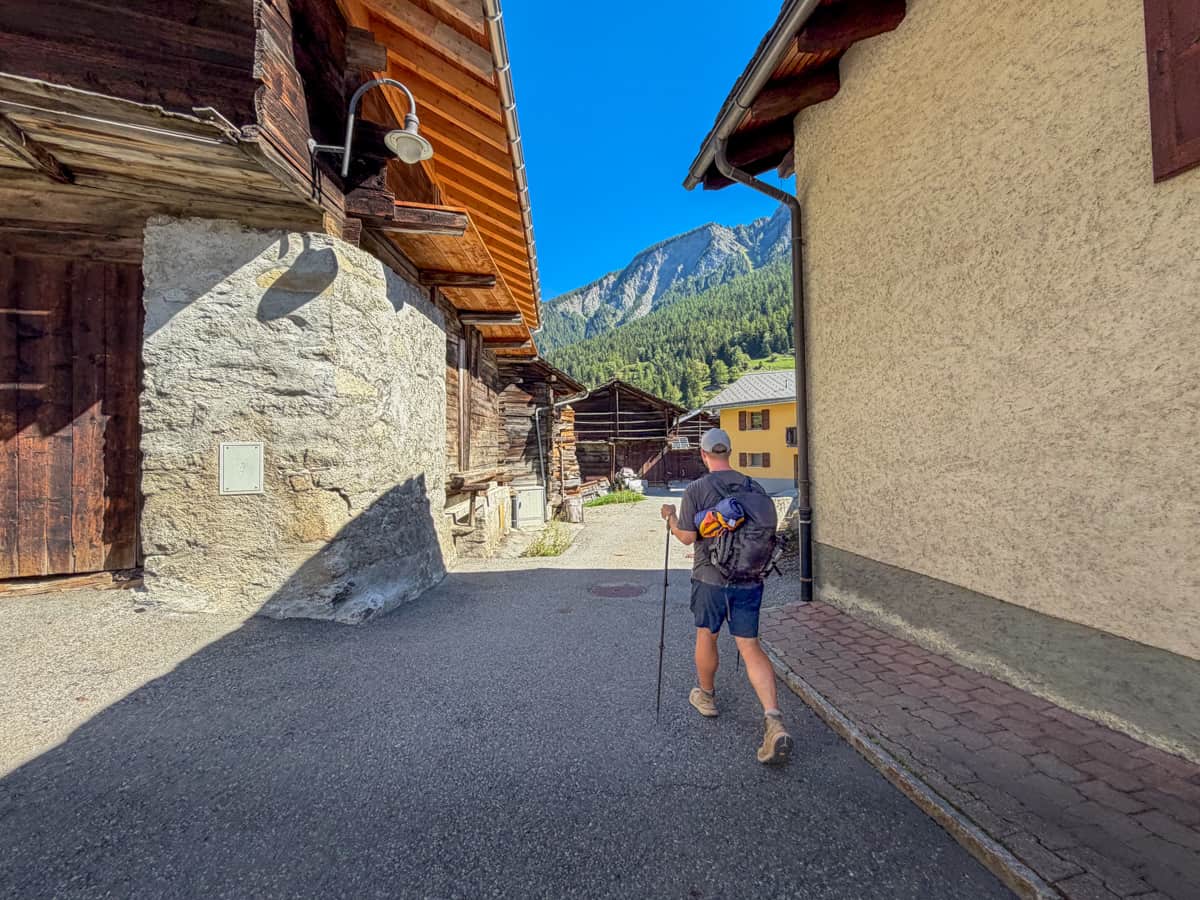 Man hiking along a pathway through wooden chalets in Switzerland along the Tour du Mont Blanc
