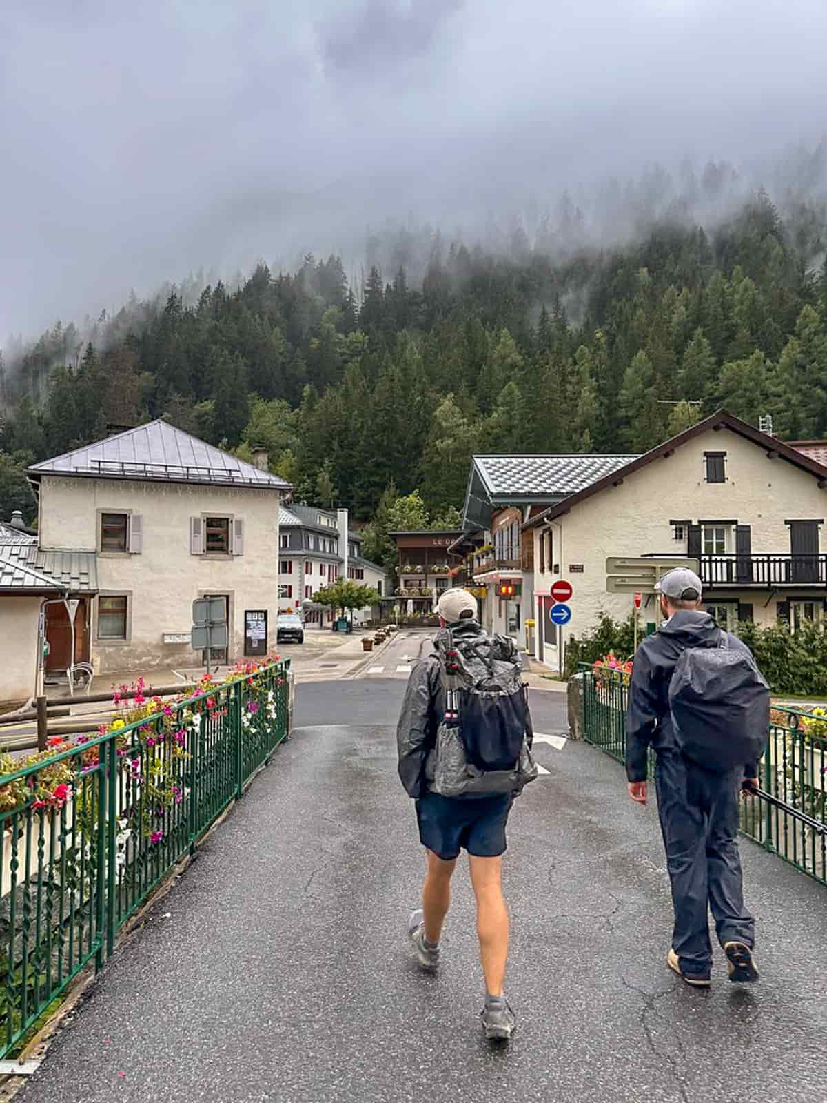 Two hikers walking through Montroc, France with a pine tree forest and gloomy clouds in the background along the Tour du Mont Blanc