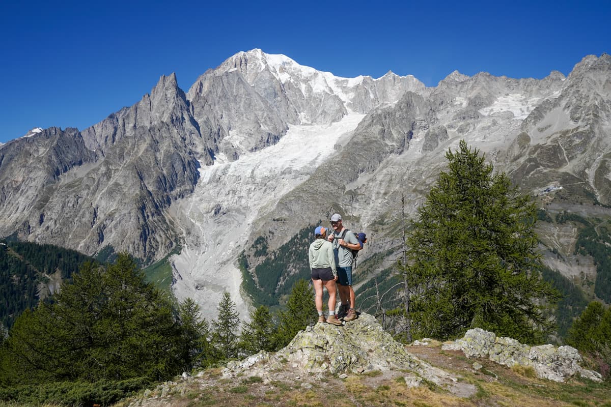 Couple standing on a rocky outcropping with the Grandes Jorasses in the background along the Val Ferret along the Tour du Mont Blanc