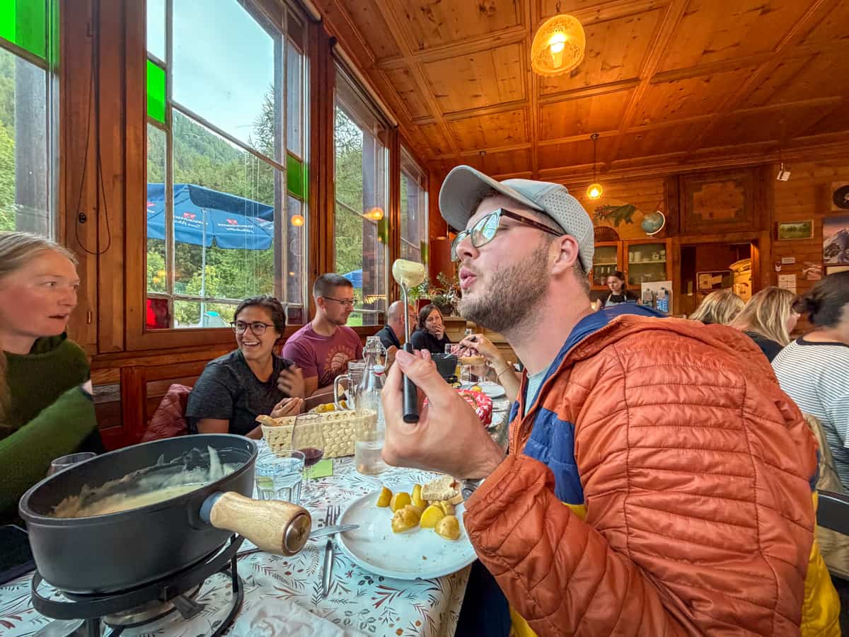 Man blowing on a cheesy potato from fondue at the Auberge Gîte Bon Abri in Champex-Lac, Switzerland along the Tour du Mont Blanc