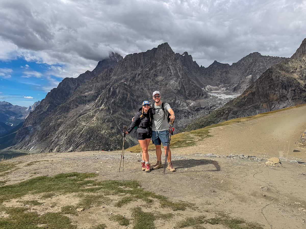 Smiling couple standing at the Grand Col Ferret with the Italian Alps in the background on the Tour du Mont Blanc