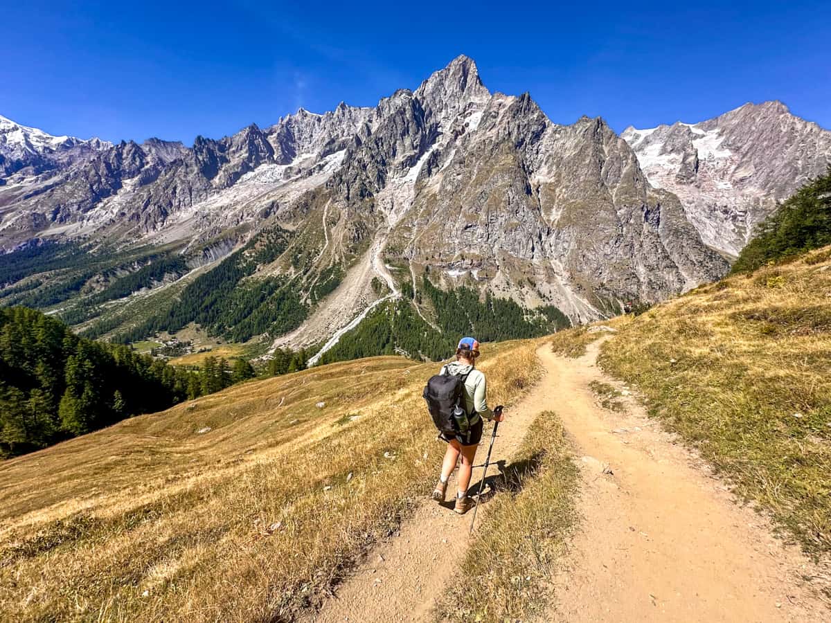 Woman hiking down a dirt pathway with the Italian Alps in the background near Rifugio Bonatti along the Tour du Mont Blanc