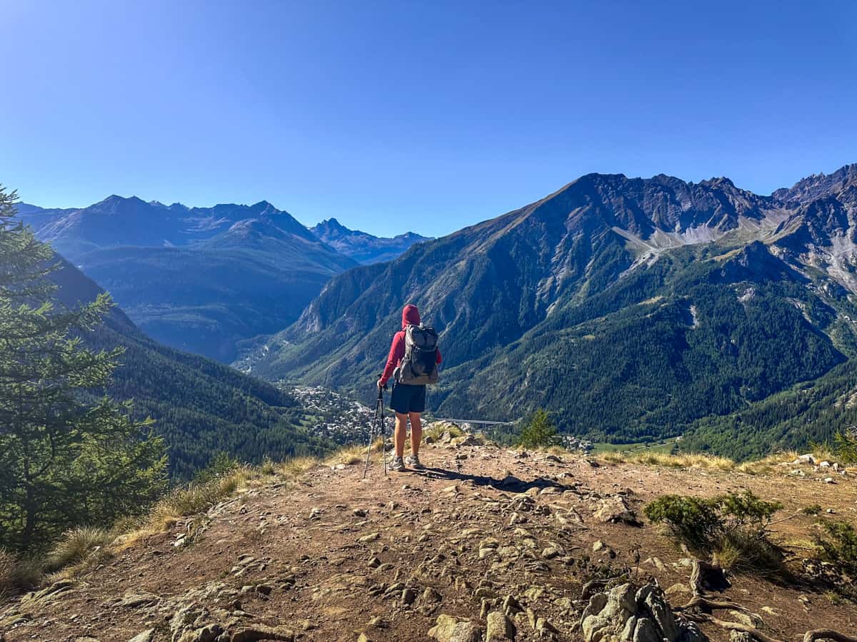 Man standing on a mountain ridge along the Val Ferret, overlooking Courmayeur, Italy and the surrounding Alps, along the Tour du Mont Blanc