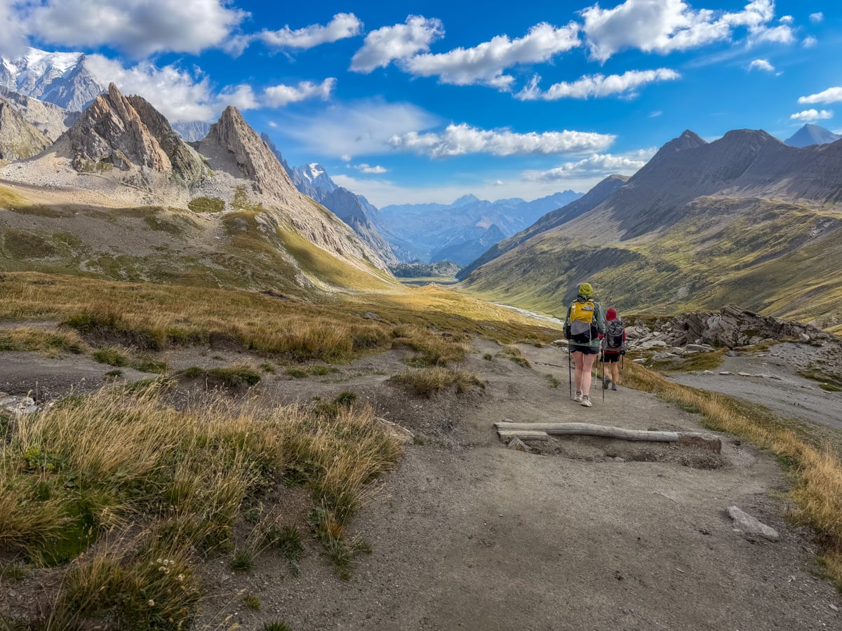 Hikers walking downhill with the Italian Alps in the background along the Tour du Mont Blanc