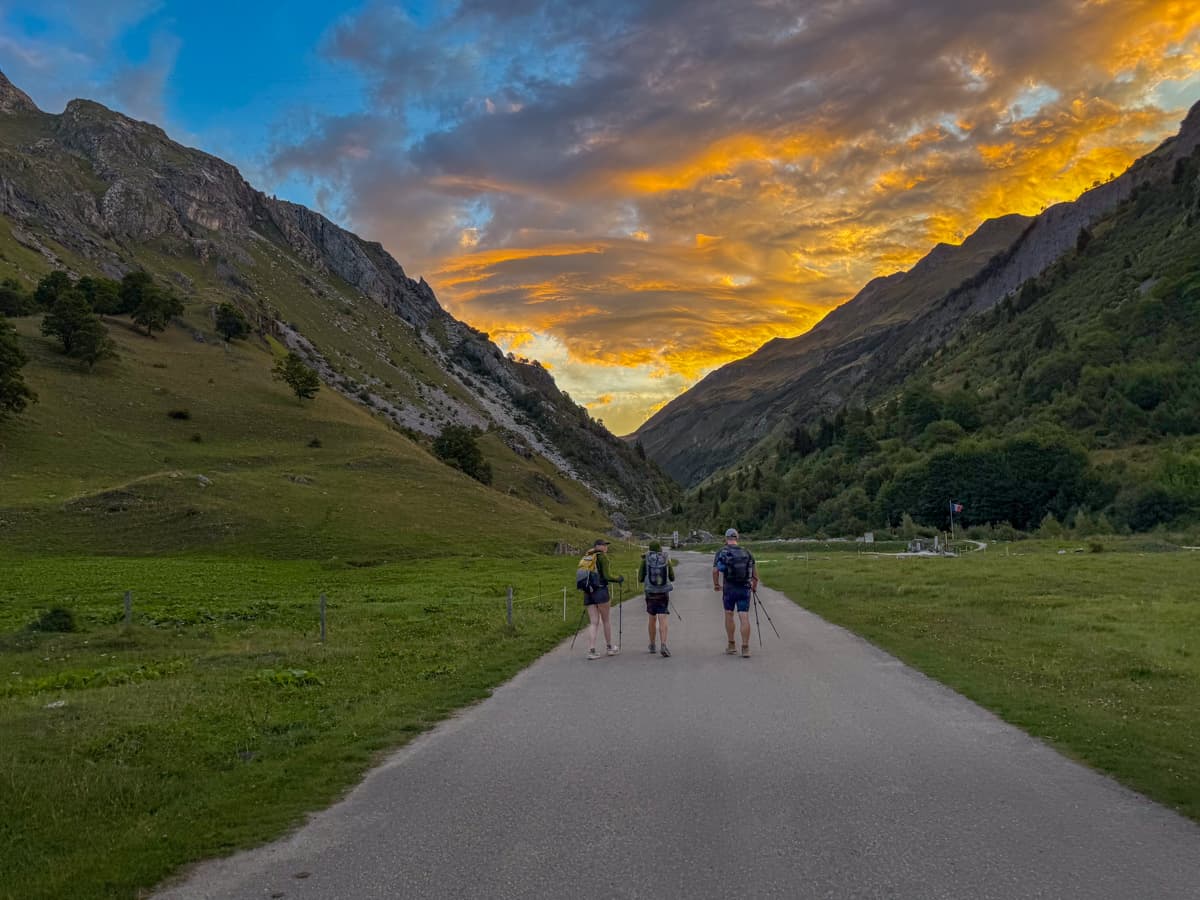 Three hikers walking along a roadside at sunrise outside of Les Chapieux, France along the Tour du Mont Blanc