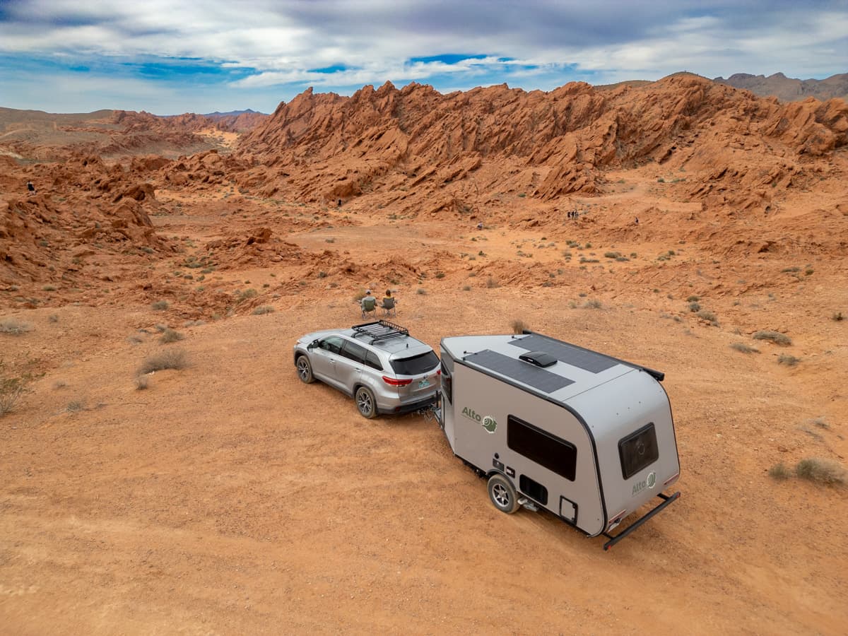 Couple sitting next to their Highlander Hybrid SUV towing a Safari Condo Alto A1752 with red rock formations in the background in the desert of Nevada