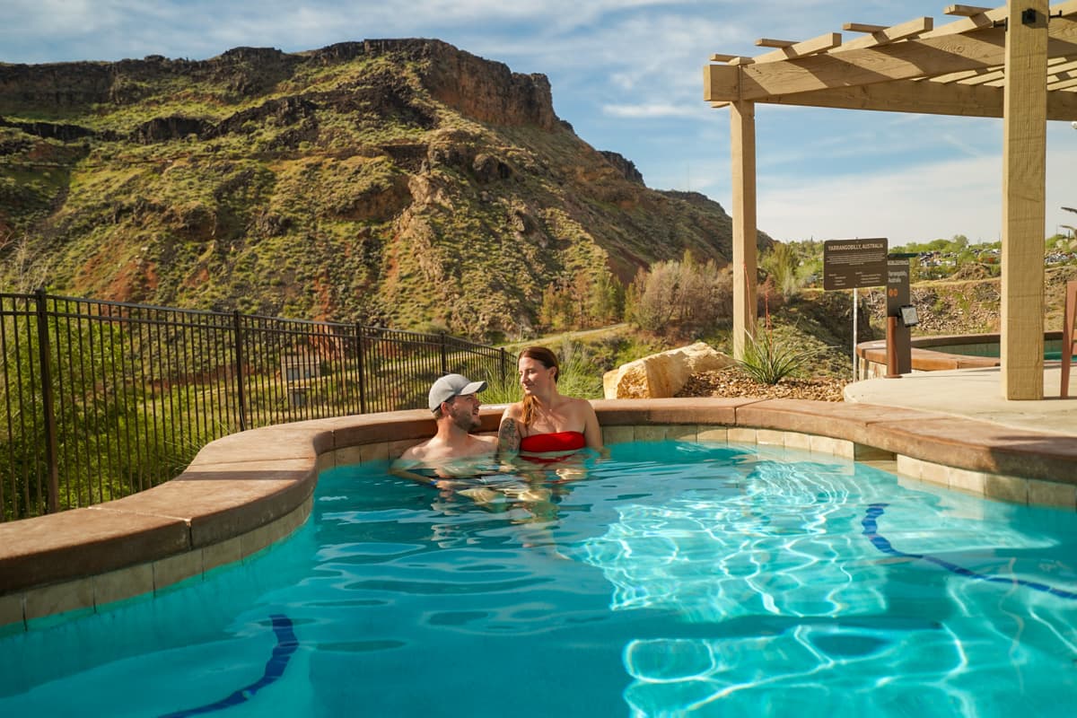 Couple sitting in a pool in Zion Canyon Hot Springs with a red rock cliff in the background in La Verkin, Utah