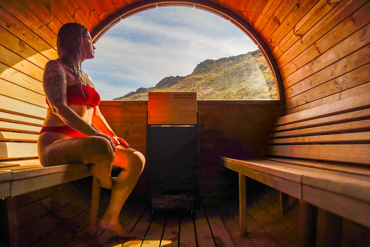 Woman sitting in a barrel sauna with red rock cliffs in the background at Zion Canyon Hot Springs in La Verkin, Utah